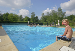 Dreng sidder ved swimmingpoolens kant på Residence De Eese 22, en lodge i Holland, omgivet af natur.