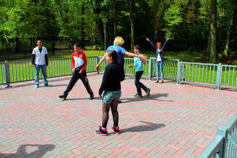Een groep tieners speelt en amuseert zich buiten op een glampingverblijf omringd door groene bomen.