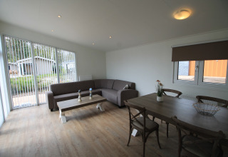 Woonkamer in chalet Residence de Eese 20 in Nederland met hoekbank, eettafel en grote ramen.