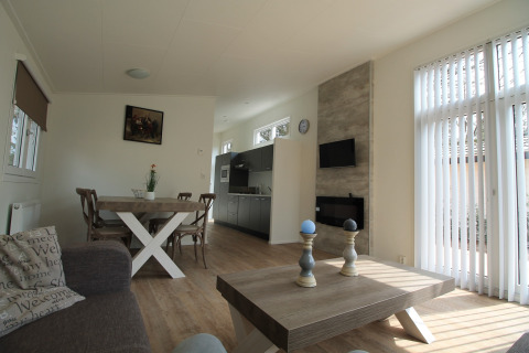 Modern chaletinterieur met eettafel, bank, groot raam en houten vloer bij Residence de Eese 20, Nederland.