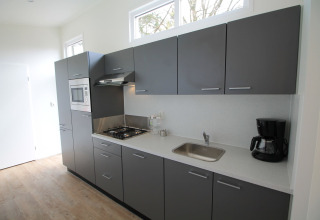 Moderne keuken met grijze kasten, gaskookplaat, magnetron, gootsteen en koffiemachine in Residence de Eese 20, Nederland.