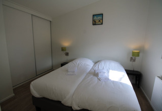 Slaapkamer met twee eenpersoonsbedden, wit beddengoed, nachtkastjes en groene lampen in Residence de Eese 20, Nederland.