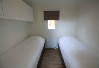 Kleine slaapkamer in Residence de Eese 20, Nederland, met twee eenpersoonsbedden en witte kasten.