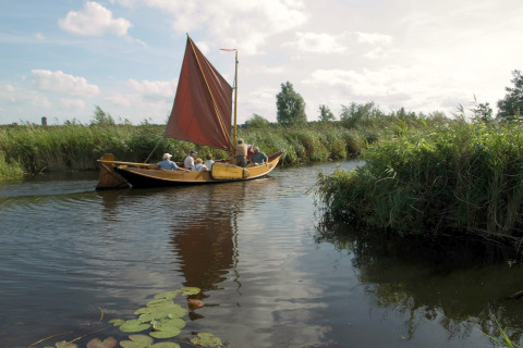 Groep mensen zeilt met een houten boot door een groen waterrijk gebied bij een glampingsite in de natuur.