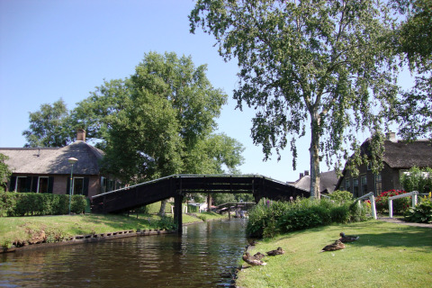 Prachtig uitzicht op het kanaal bij Residence De Eese 22 lodge in Nederland met brug en eenden op het gras.