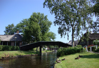 Idyllisk kanaludsigten ved Residence De Eese 22 lodge i Holland med bro, træer og ænder på græsset.
