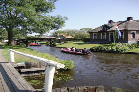 Kanaal aan Residence De Eese 22 in Nederland, met bootjes, een huis en een wapperende Nederlandse vlag.