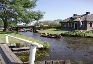Kanaal aan Residence De Eese 22 in Nederland, met bootjes, een huis en een wapperende Nederlandse vlag.