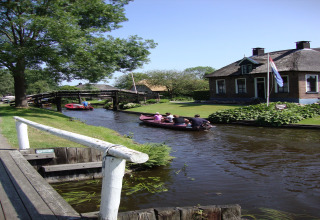Idyllisk kanal ved Residence De Eese 22 i Holland med mennesker i både og et charmerende hus med flag.