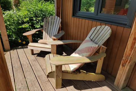 Two wooden chairs on a sunny porch at a tiny house for two people in the Netherlands, with greenery.