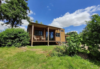 Tiny house for 2 persons in the Netherlands, set among greenery with a covered porch under blue skies.