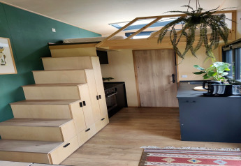 Interieur van een moderne tiny house in Nederland met trap naar de slaapzolder, keuken en hangplanten.