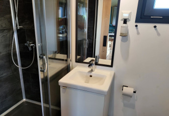 Modern compacte badkamer met douchecabine, kleine wastafel, spiegel en wc-rolhouder in een Tiny House.