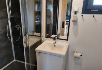 Compact modern bathroom with shower cabin, small sink, mirror, and toilet paper holder in a Tiny House.