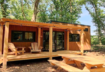 Klein houten huisje met veranda, twee stoelen en picknicktafel in een bos in Nederland.