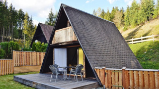 A-frame wooden cabin with terrace and outdoor seating at Ferienhütte Trabochersee, surrounded by trees.
