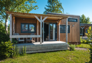 Pequeña casa de madera con porche y dos sillas, Tiny House para 2 personas en un entorno holandés verde.