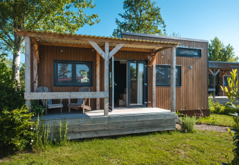Small wooden tiny house with porch and two chairs, Tiny House for 2 persons, in a green Dutch setting.