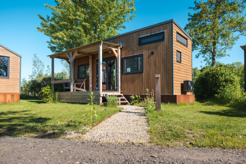 Photo of a wooden tiny house named Tiny House for 2, suitable for two persons, set in a green area.