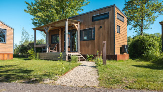 Photo of a wooden tiny house named Tiny House for 2, suitable for two persons, set in a green area.