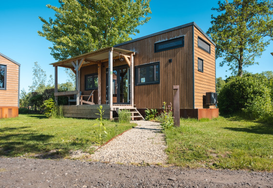 Photo of a wooden tiny house named Tiny House for 2, suitable for two persons, set in a green area.