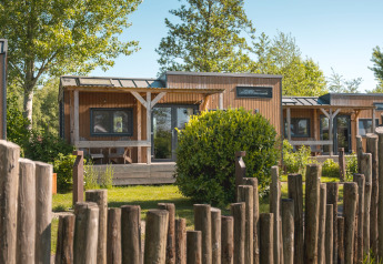 Knus houten tiny house voor 2 personen in Nederland, met groene tuin en rustiek houten hekwerk.