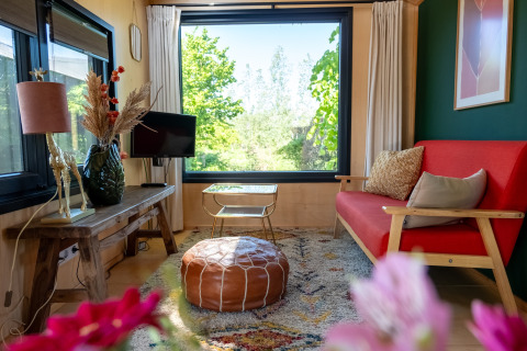 Salón de una tiny house para 2 personas en Países Bajos, con sofá rojo y ventana grande con vista.