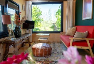 Salón de una tiny house para 2 personas en Países Bajos, con sofá rojo y ventana grande con vista.