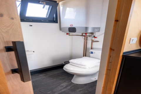 Petite salle de bain avec toilettes, serviette et chauffe-eau dans tiny house pour 2 personnes aux Pays-Bas.
