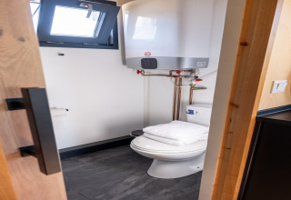 Compact bathroom with toilet, towel on seat, and water heater in a tiny house for 2 people in the Netherlands.
