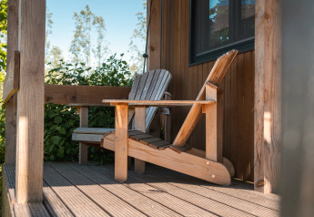 Adirondack-stoel op de veranda van Tiny House for 2 in Nederland, omgeven door groen.
