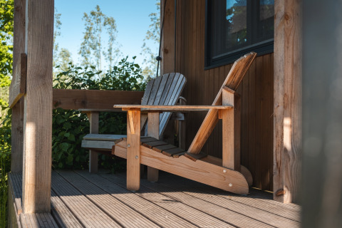 Adirondack chair on the porch of Tiny House for 2 in the Netherlands, surrounded by greenery.