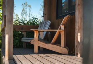 Silla Adirondack en el porche de Tiny House for 2 en los Países Bajos, rodeada de vegetación verde.