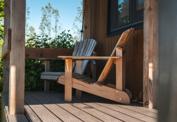 Adirondack chair on the porch of Tiny House for 2 in the Netherlands, surrounded by greenery.