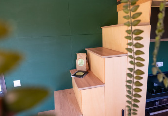 Wooden stairs in a tiny house with green wall, coffee, notebook, and hanging plant, Tiny House Netherlands.
