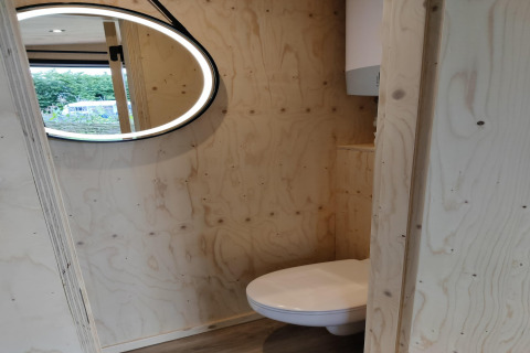 Badkamer met houten wanden, hangtoilet en modern verlicht spiegel in Wetland Cabin, Nederland.