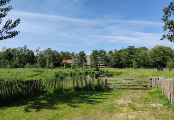 Pradera verde con valla de madera y cabaña bajo cielo azul en Wetland Cabin, Friesland, Países Bajos.