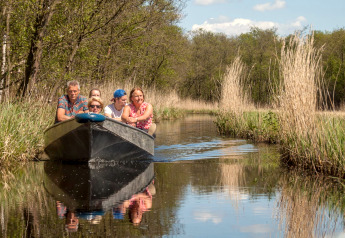 En gruppe mennesker sejler i en båd gennem en smal kanal omgivet af natur ved Large Green House i Holland.