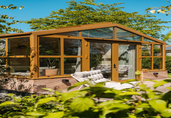 Buitenfoto van het verblijf ‘Large Green House 4 persons’ in Nederland met veel glas en ligzetel buiten.