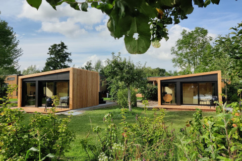 Two modern wooden cabins with large windows in a lush garden at Boetiekpark de Kas, Scherpenzeel, Friesland.