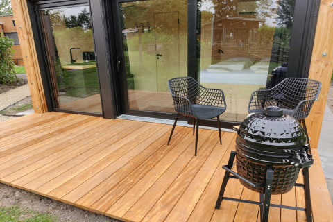 Wooden deck with two black chairs and a barbecue outside Wetland Cabin for 2 at Boetiekpark de Kas, Netherlands.