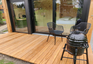 Houten terras met twee zwarte stoelen en barbecue bij Wetland Cabin voor 2 personen in Friesland, Nederland.