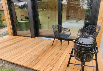Terrasse en bois avec deux chaises noires et un barbecue devant la Wetland Cabin pour 2 personnes, Friesland, Pays-Bas.