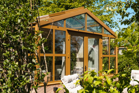 Lodge di vetro soleggiato con cornici dorate in un giardino verde, Large Green House 4 persons, Paesi Bassi.