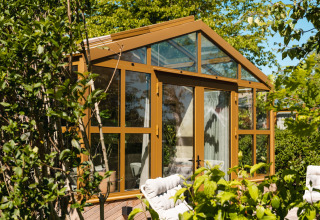 Lodge di vetro soleggiato con cornici dorate in un giardino verde, Large Green House 4 persons, Paesi Bassi.
