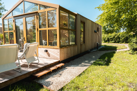 Esterno della lodge Large Green House per 4 persone con terrazza in legno e sedie da giardino al sole.
