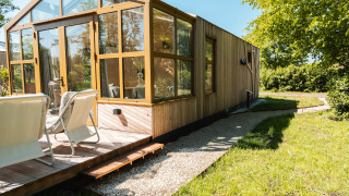 Buitenzijde van Large Green House lodge voor 4 personen met houten terras en stoelen in de zon.
