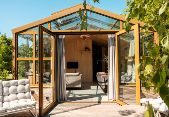 Stort glashus-lodge med åbne døre, sollys og moderne indretning i naturskønne omgivelser i Holland.