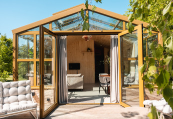 Grote glazen lodge met open deuren, gezellig interieur en natuurlijke omgeving in Nederland.