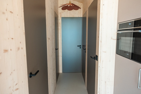 Corridoio con pareti in legno chiaro, quattro porte e arredi moderni nel lodge Large Green House 4 persone nei Paesi Bassi.